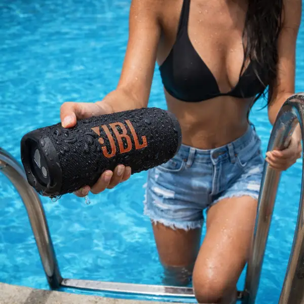 JBL Flip 7 preta na horizontal mostrando os radiadores de graves laterais.