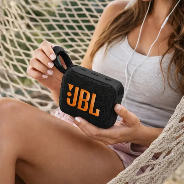 Caixa de som JBL Go 4 preta resistente à água sobre superfície molhada.